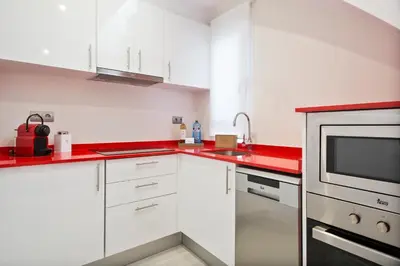 a kitchen with white cabinets and red counter tops at Sitges Group Blue&White in Sitges