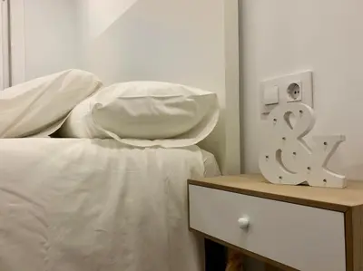 a bed with white sheets and a alarm clock on a table at MonResidence Cavall Bernat in Manresa