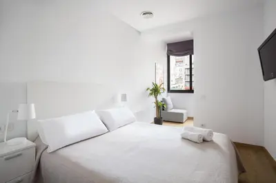 a white bedroom with a white bed and a chair at Stay U-nique Apartments Villarroel in Barcelona
