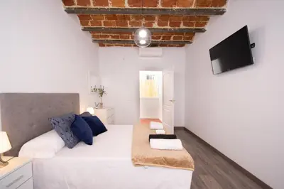 a white bedroom with a large bed and a flat screen tv at Apartahotel Casa Batito in Hospitalet de Llobregat