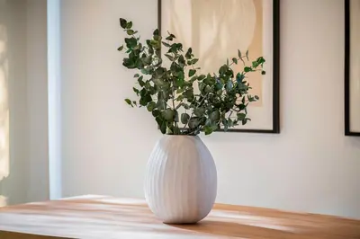 a white vase with a plant in it on a table at ApartsNouBcn Equador Les Corts in Barcelona