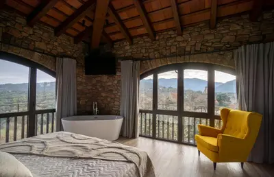 a bedroom with a tub and a chair and windows at Alojamiento MAS EL CASTELL DEL BRULL B&B in El Brull