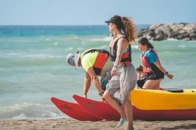a woman helping a man on a paddle board on the beach at Tres Estrellas Barcelona by HolaCamp in Gavà