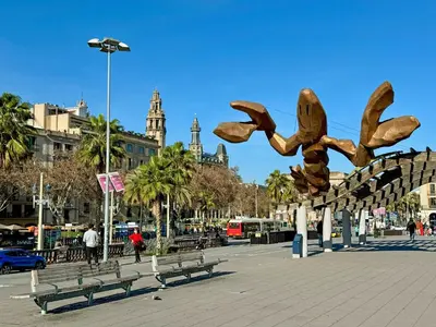 a sculpture in a plaza with benches and buildings at Colom Apartment 3BR with Balcony & Port Vell Views in Barcelona