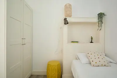 a bedroom with a white bed and a yellow stool at Casa Cosi - Francoli 4 in Barcelona
