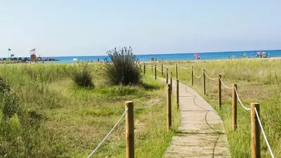 a wooden path to the beach with people in the background at Onze - primera línea de mar con piscina in Cubelles