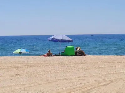 two people sitting under an umbrella on the beach at Bright with pool near the beach and Barcelona by train in Masnou