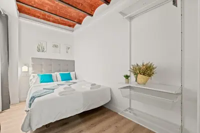 a white bedroom with a large bed with blue pillows at Tendency Apartments 5 in Barcelona