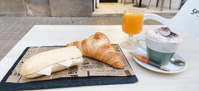 a table with a cup of coffee and a croissant and a drink at Hostal Live Natura Barcelona in Barcelona