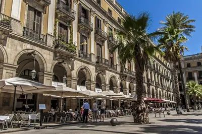 a building with tables and umbrellas and a palm tree at Habitat Apartments Art in Barcelona