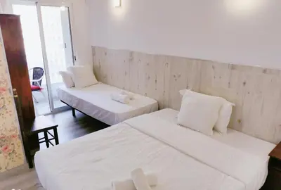 a room with two beds and a chair and a window at Barcelona CoronaHostal in Badalona