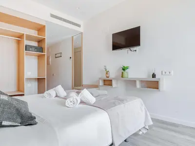 a white bedroom with two beds and a flat screen tv at Limehome Barcelona Carrer de Besalú 82 in Barcelona