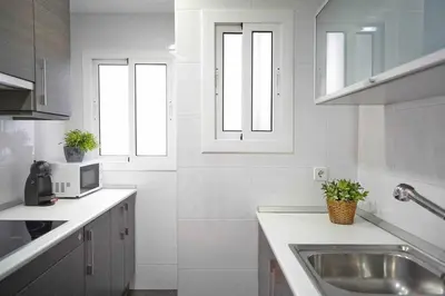 a white kitchen with a sink and two windows at SAGRADA FAMILIA VIEWS Nos preocupa su seguridad. in Barcelona
