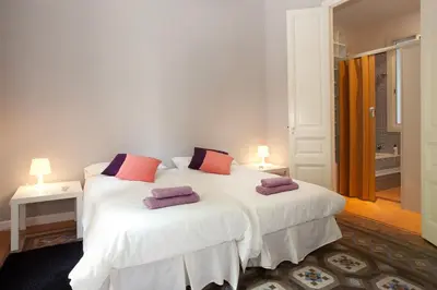 a bedroom with two beds with white sheets and purple pillows at Modernist Apartment Barcelona in Barcelona