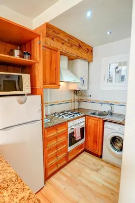 a kitchen with wooden cabinets and a white refrigerator at Hermione Apartment by Hello Homes Sitges in Sitges