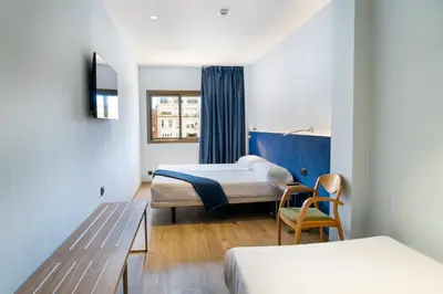 a hotel room with two beds and a chair at Caledonian in Barcelona