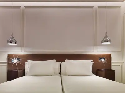 a bedroom with two beds with white sheets and two lights at H10 Itaca in Barcelona