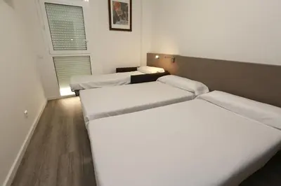 a room with three beds and a window at Hotel Alguer Camp Nou in Barcelona
