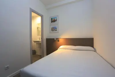 a large white bed in a room with a bathroom at Hotel Alguer Camp Nou in Barcelona