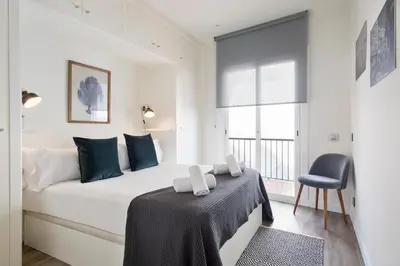 a white bedroom with a bed and a chair at Sitges Group Ocean in Sitges