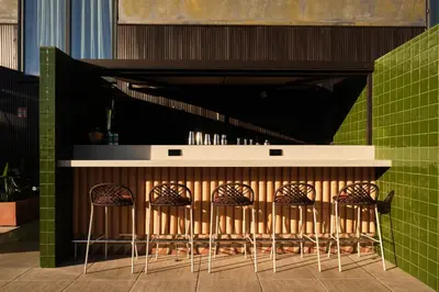 a bar with four stools in front of a green wall at Catalonia Gran Hotel Verdi in Sabadell