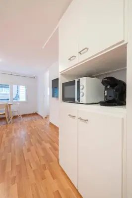 a white kitchen with white cabinets and a wooden floor at Homenfun Barcelona Park Güell in Barcelona