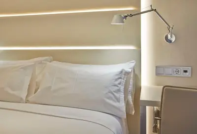 a bed with white sheets and a lamp next to it at NH Barcelona Les Corts in Barcelona