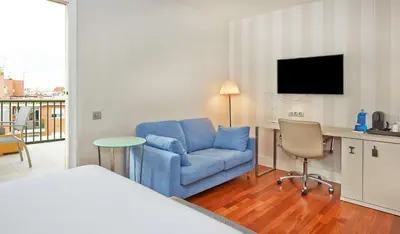 a room with a blue chair and a desk with a tv at NH Barcelona Les Corts in Barcelona