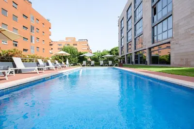 a large swimming pool with chairs and buildings at Sercotel Cornellà Barcelona in Cornellà de Llobregat