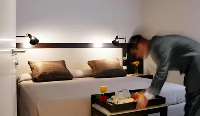 a man standing in front of a bed with a tray of food at Park Hotel in Barcelona