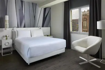 a bedroom with a white bed and a white chair at NH Barcelona Stadium in Barcelona
