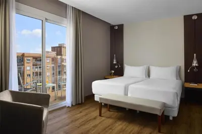 a bedroom with a white bed and a large window at NH Barcelona Stadium in Barcelona