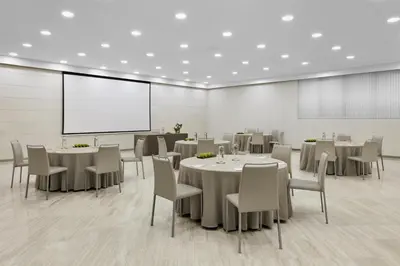 a conference room with tables and chairs and a screen at NH Barcelona Stadium in Barcelona