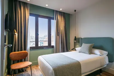 a bedroom with a bed and a window and a chair at Hotel Via Augusta in Barcelona
