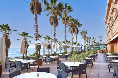 an outdoor patio with tables and chairs and the ocean at Sunway Playa Golf & Spa Sitges in Sitges