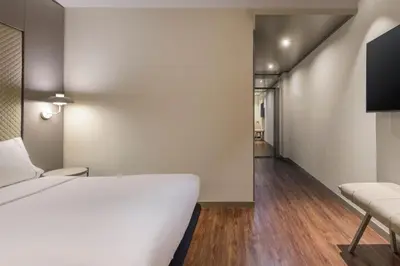 a bedroom with a white bed and a hallway at AC Hotel Som by Marriott in Hospitalet de Llobregat