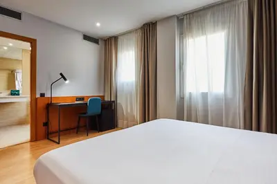 a bedroom with a bed and a desk and a window at Silken Sant Gervasi in Barcelona