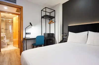 a bedroom with a bed and a desk and a blue chair at Silken Sant Gervasi in Barcelona