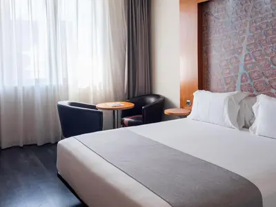 a hotel room with a bed and chairs and a window at Abba Sants in Barcelona