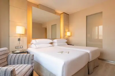 a large white bed in a room with two chairs at Hesperia Barcelona Presidente in Barcelona