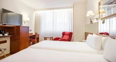 a hotel room with a white bed and a desk at Ilunion Les Corts Spa in Barcelona