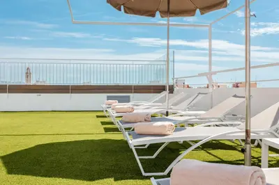 a row of lounge chairs and an umbrella on a roof at DWO Les Palmeres in Calella