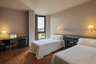 a hotel room with two beds and a desk and a window at Ciutat de Granollers in Granollers