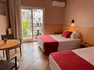 a hotel room with two beds and a table and a window at Hotel Piccadilly Sitges in Sitges