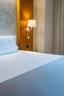 a bed in a hotel room with a white bedspread and a lamp at Abba Rambla Hotel in Barcelona