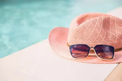 a straw hat and sunglasses sitting next to a swimming pool at Hyatt Regency Barcelona Tower in Hospitalet de Llobregat