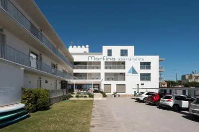 a large white building with cars parked in a parking lot at Apartamentos Marfina in Castelldefels
