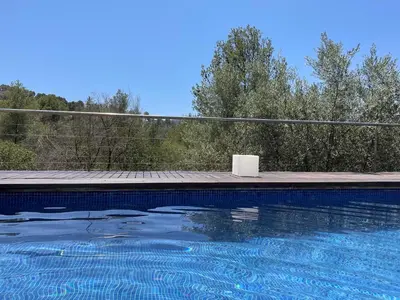 a blue swimming pool with a fence and trees at Sunny forest Villa near Barcelona in Vallirana
