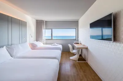a hotel room with two beds and a desk and a television at Occidental Atenea Mar - Adults Only in Barcelona