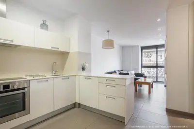 a white kitchen with white cabinets and a living room at Flateli Navas D01 in Barcelona